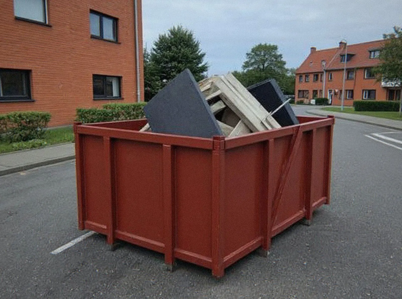 Benne rouge pleine d'encombrants au bord d'une rue, prête à être reprise par MOL Bennes à Molsheim